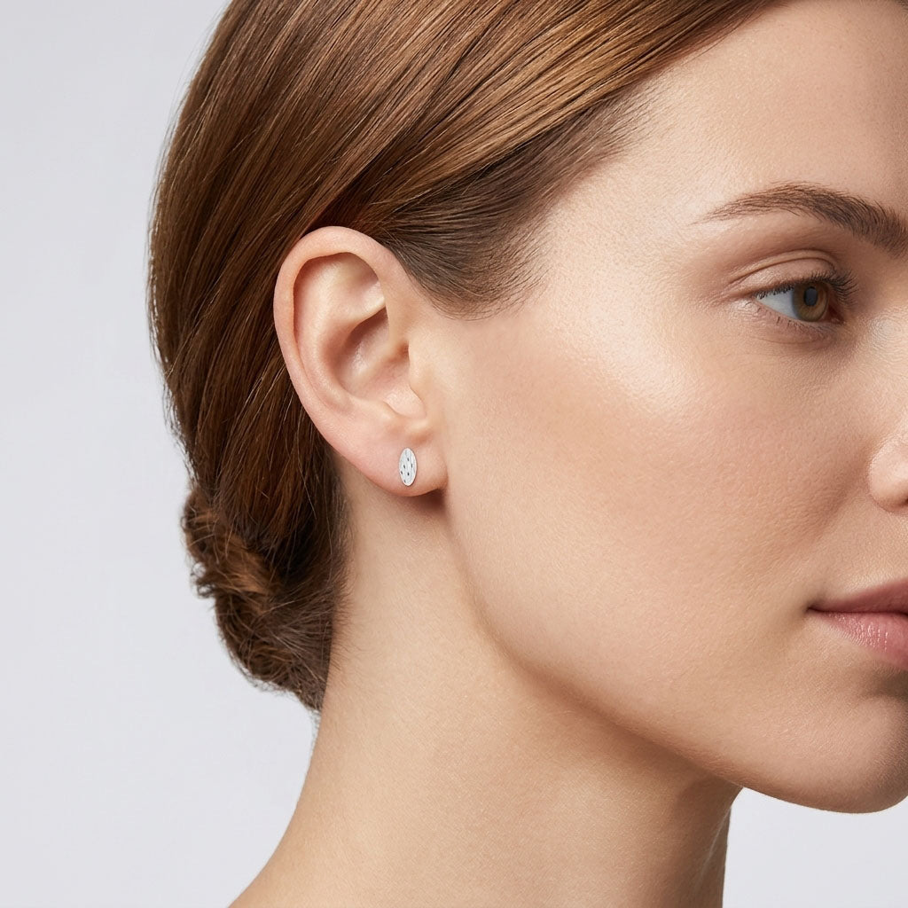 Овальная серьга-гвоздик серебристого тона с рельефным узором в ухе модели