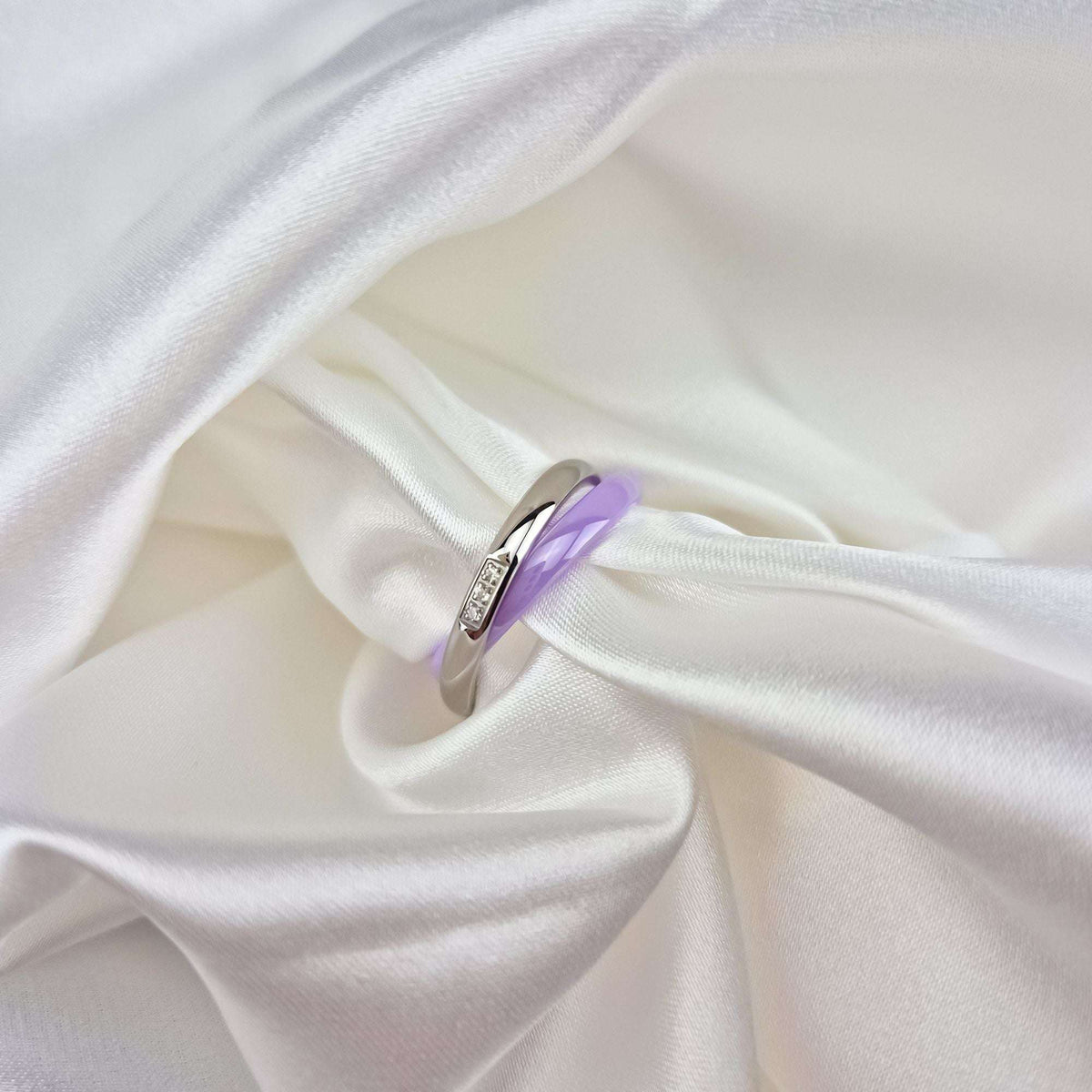 Violetais keramikas gredzens ar platīna pārklājumu tuvplānā uz balta zīda auduma krokām